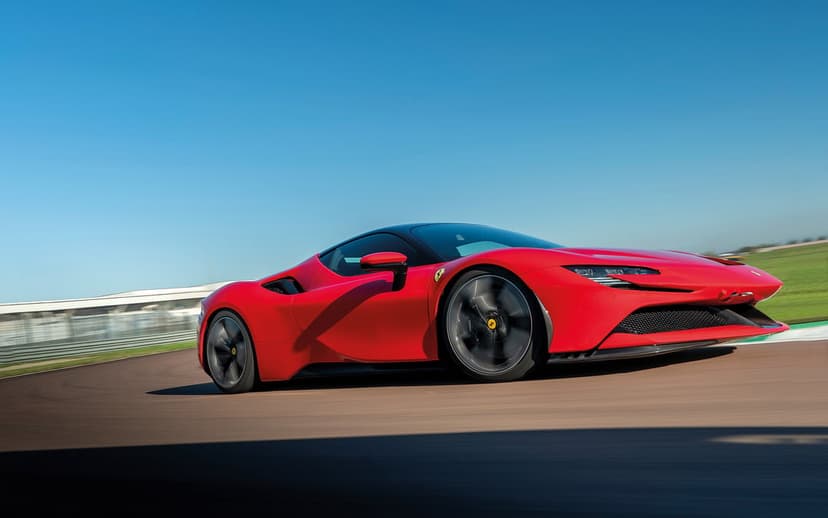 Red Ferrari SF90 Stradale supercar racing on an asphalt track with motion blur under a bright clear blue sky.