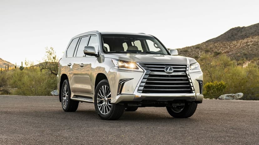 Silver Lexus LX 570 luxury SUV on a desert road at sunset with mountains and dry brush in the background.