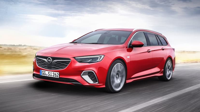 Red station wagon driving fast on a paved road with blurred wheels under a bright overcast sky background.