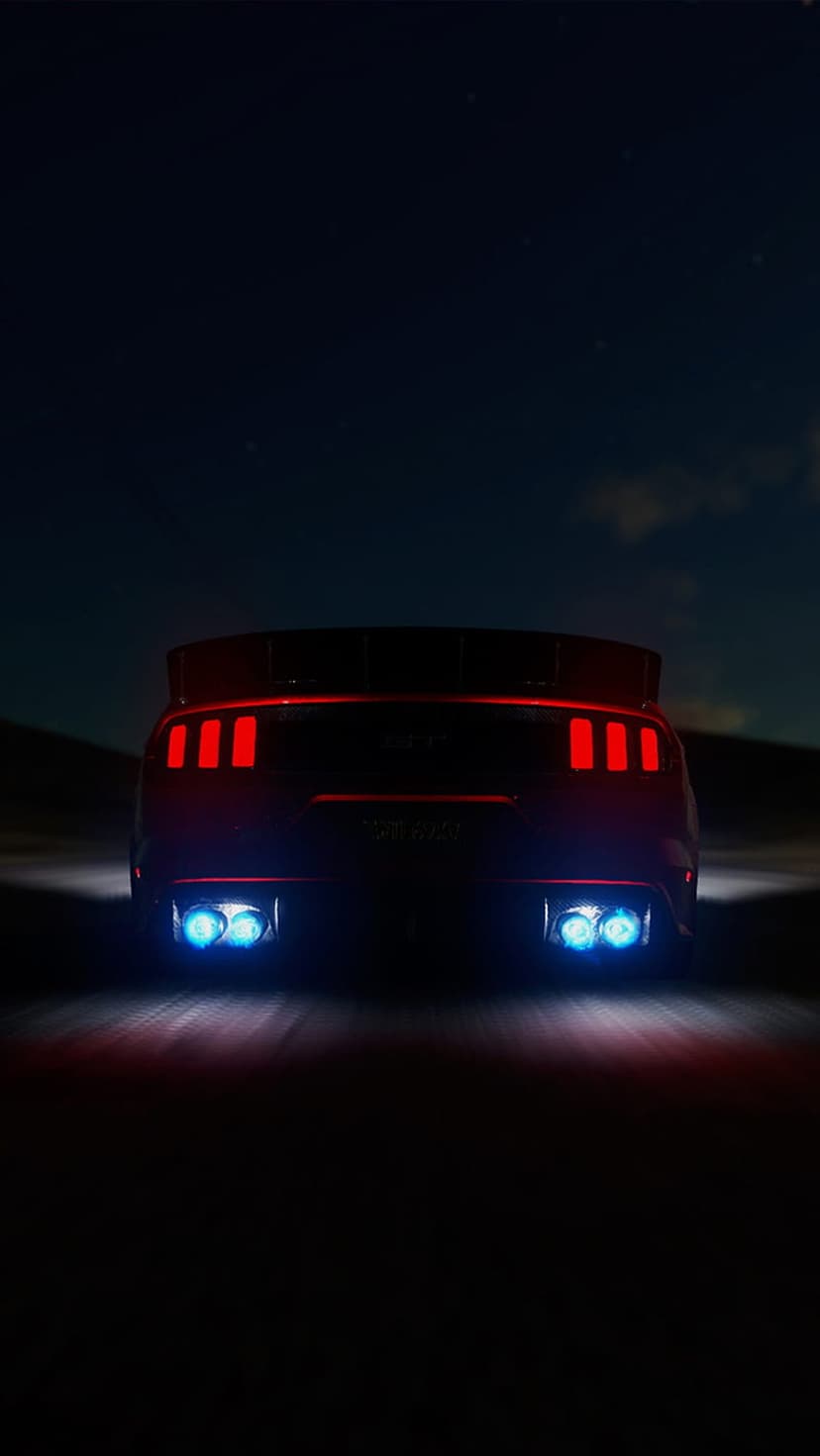 Ford Mustang GT rear view at night featuring glowing red tri-bar taillights and bright blue exhaust flames.