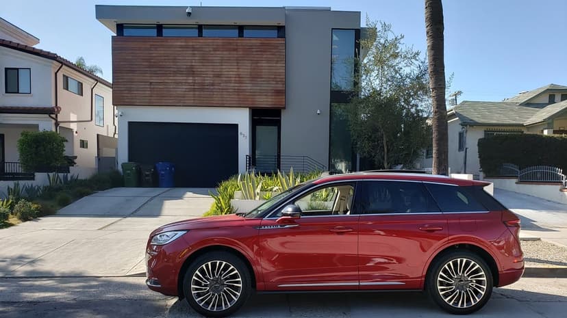Red Lincoln Corsair SUV parked in a driveway before a modern gray and wood house under a bright blue sky.