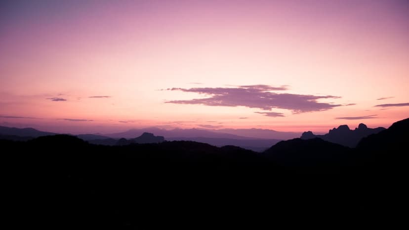 Jagged mountain silhouettes stand against a vibrant purple and pink sunset sky filled with wispy clouds.