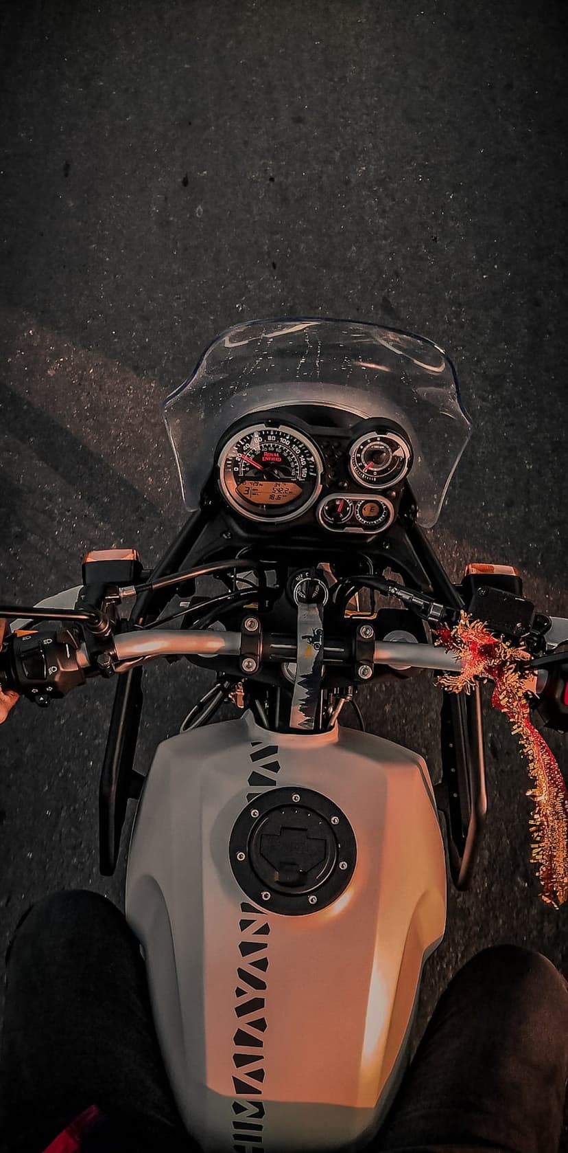 Motorcycle cockpit with analog gauges, white fuel tank with decals, and handlebars seen from a POV perspective.