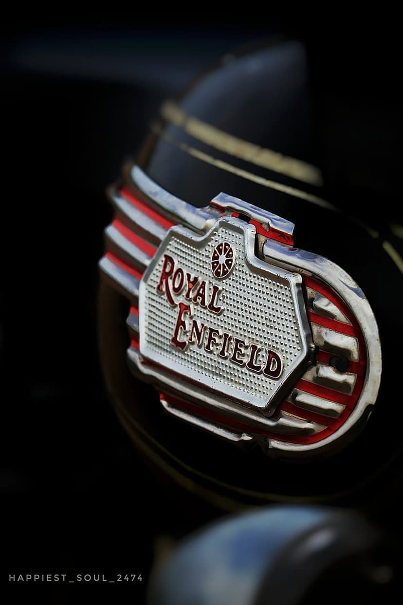 Royal Enfield chrome logo with red detailing on a dark motorcycle fuel tank under dramatic low-key lighting.