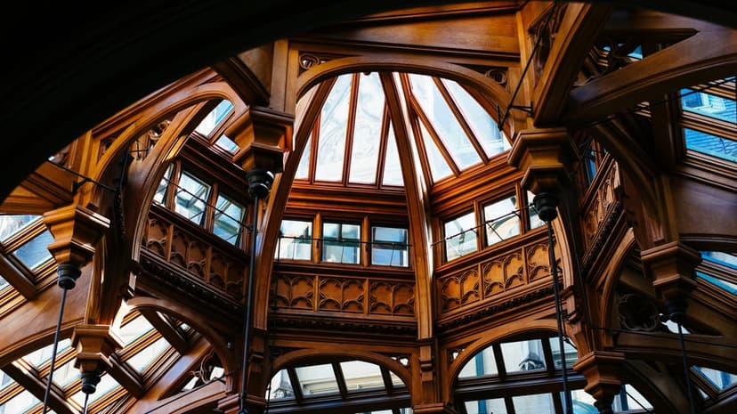 Hand-carved wooden beams and arched structures support an ornate geometric glass ceiling illuminated by sunlight.