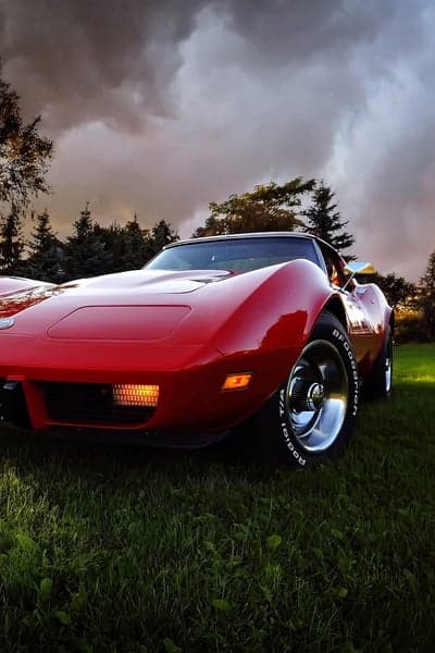Classic Red Corvette on Grassy Field Under Dramatic Sky