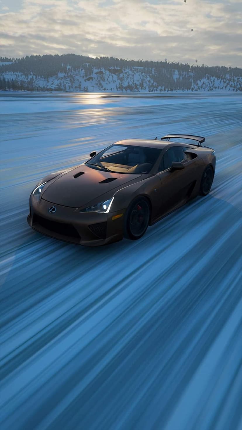 Lexus LFA supercar drifts on a frozen lake with distant hot air balloons under a cloudy, sunlit winter sky.