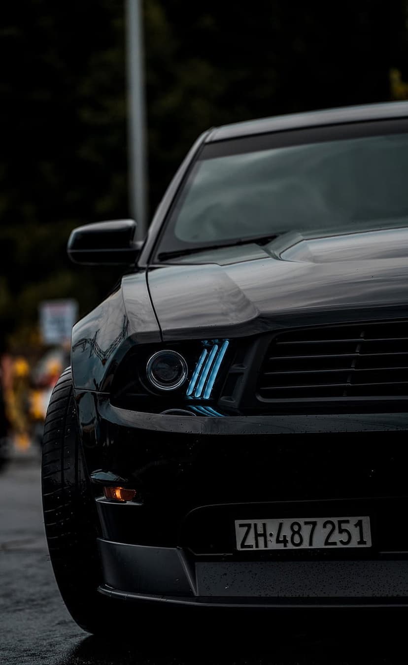 Black Ford Mustang front grille and blue LED headlights glowing in a dark, moody automotive close-up.