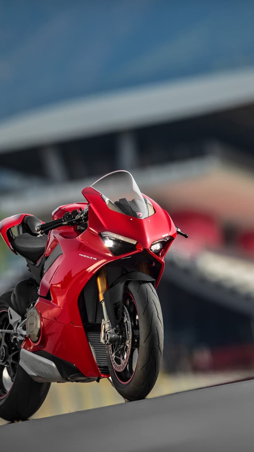 Red Ducati Panigale V4 S superbike with glowing headlights parked on a race track under a soft blue sky.