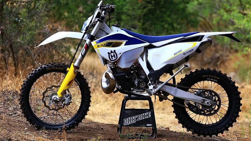 Profile of a white Husqvarna 300 TE dirt bike on a black stand against a natural outdoor background of dry brush.