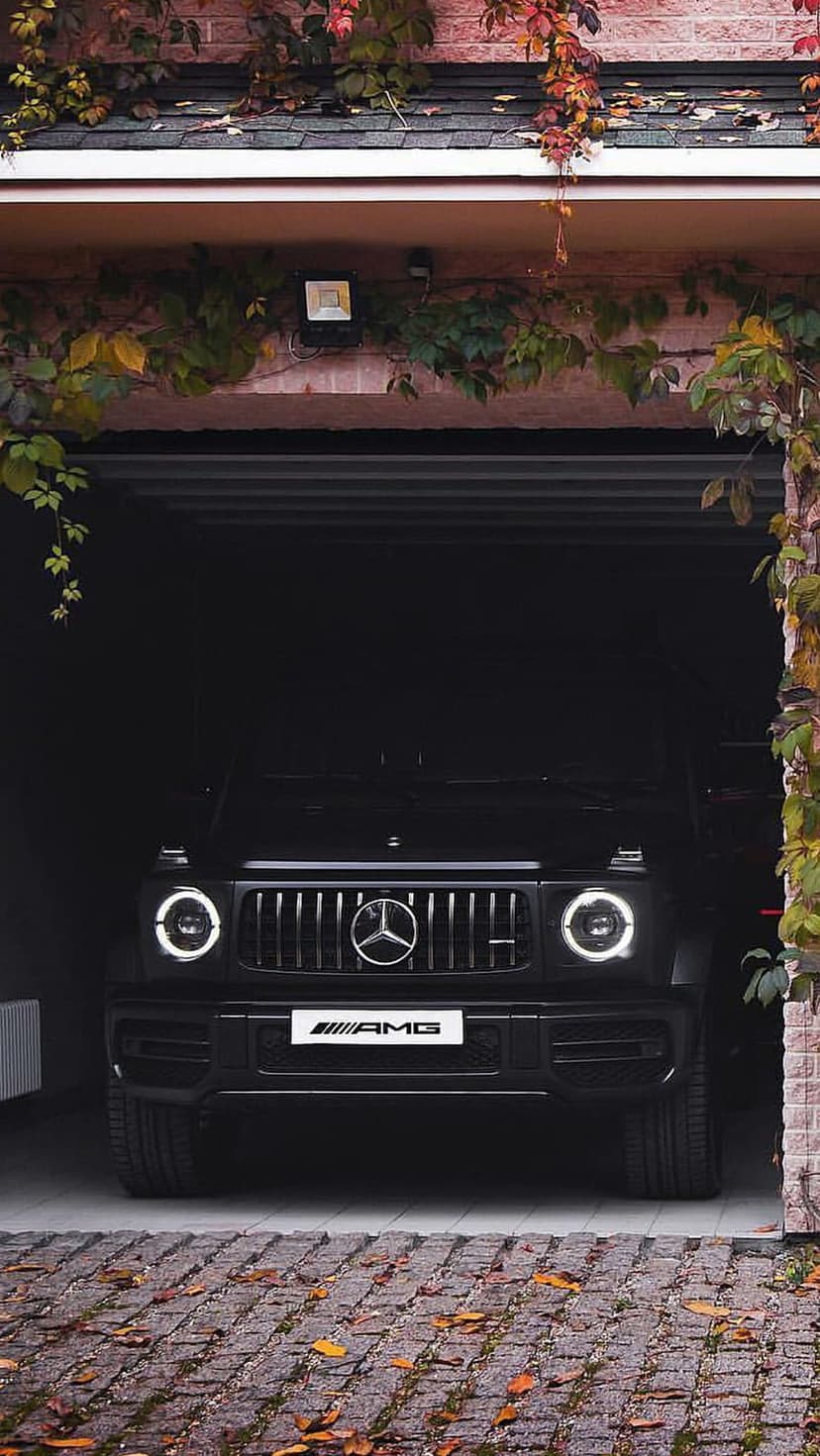 Black Mercedes-AMG G-Wagon SUV parked inside a brick garage framed by cascading red and orange autumn leaves.