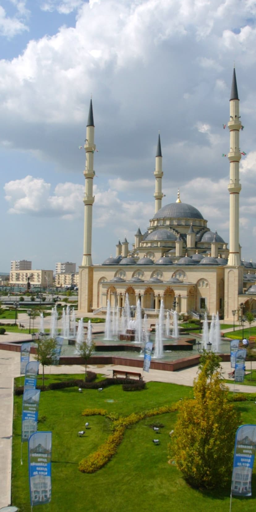 Heart of Chechnya Mosque with four tall minarets and central dome behind tiered water fountains and green gardens.