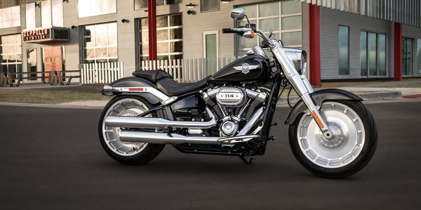 Black Harley-Davidson Fat Boy motorcycle with chrome exhaust and solid wheels parked before an industrial building.