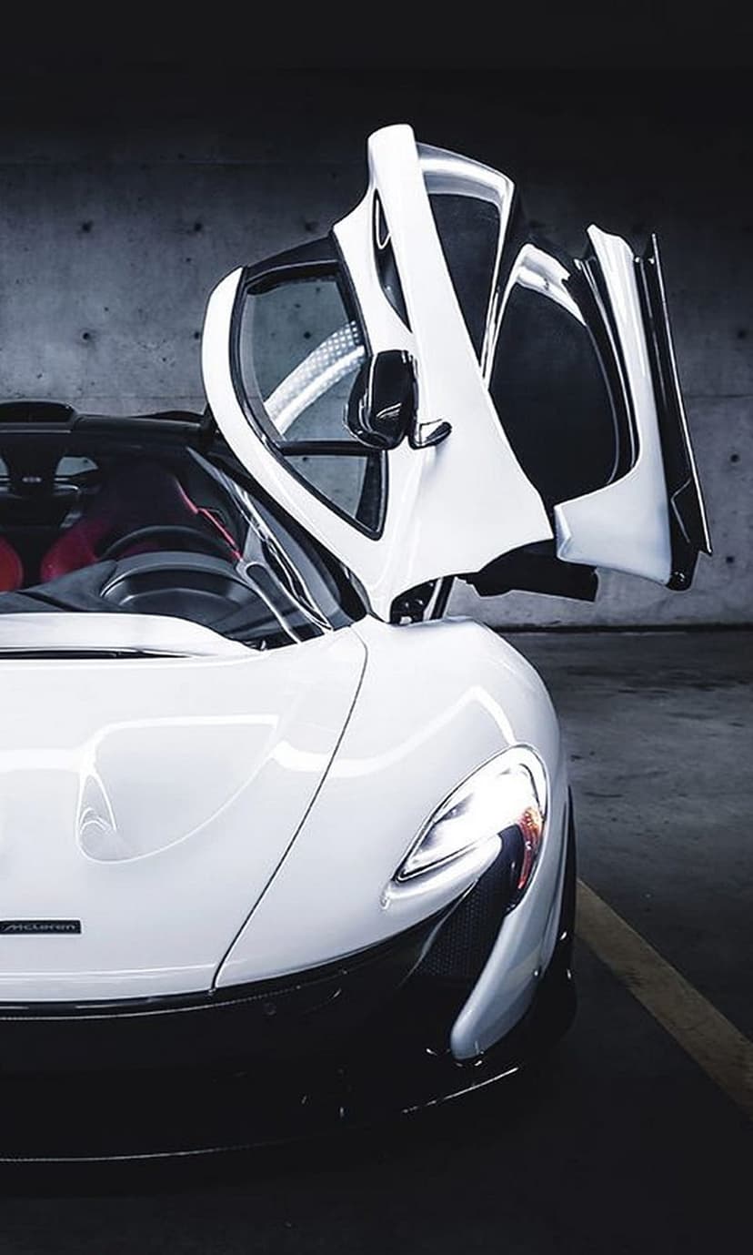 White McLaren P1 supercar with upward-opening doors revealing a red interior inside a dimly lit concrete garage.