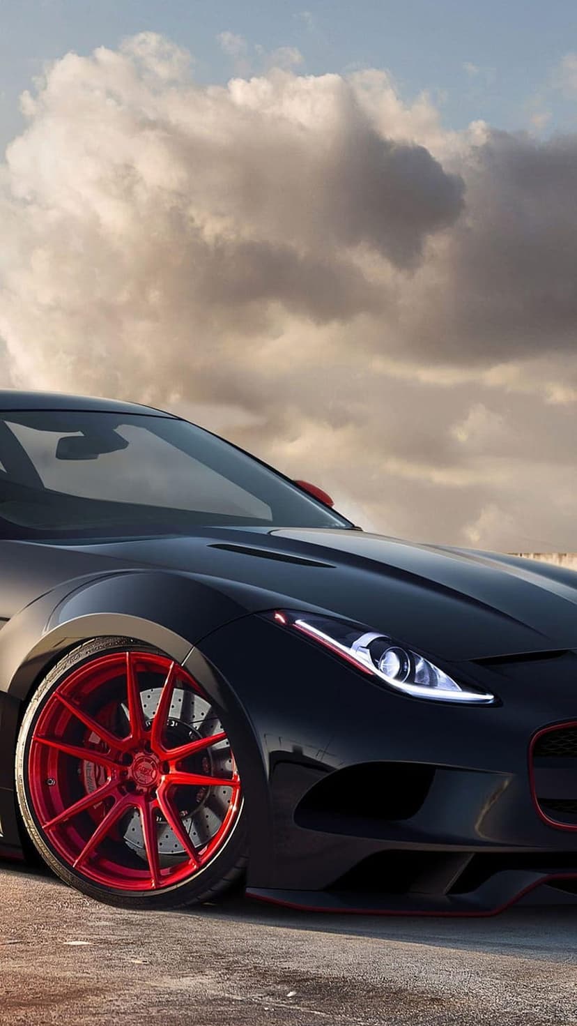 Black sports car with bright red multi-spoke wheels and glowing headlights parked beneath a dark cloudy sky.