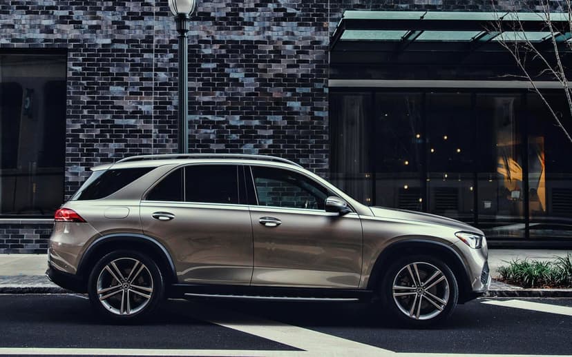 Champagne Mercedes-Benz GLE SUV parked side-on against a dark brick building and glass windows.