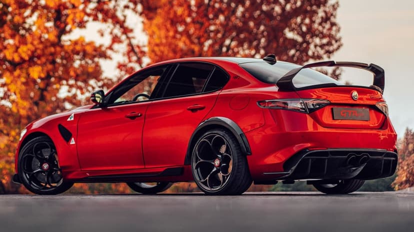 Red Alfa Romeo Giulia GTAm sports sedan with a large rear wing parked against blurred orange autumn trees.