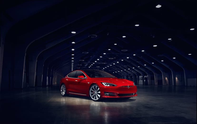 Red Tesla Model S parked in a dark hangar under dramatic overhead spotlights with reflections on the floor.