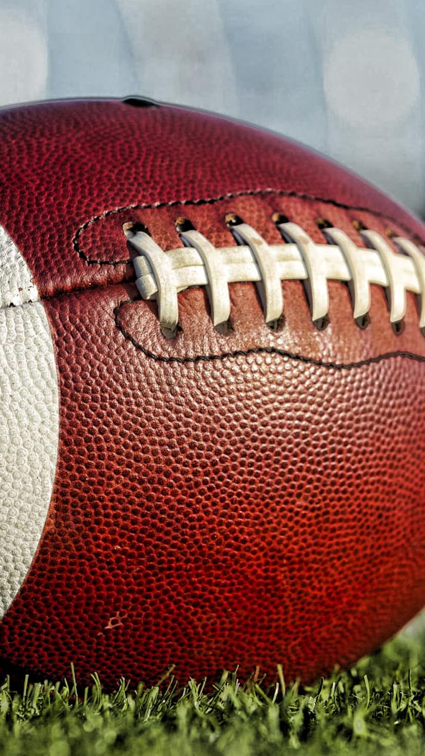 American football with white laces rests on synthetic green grass blades in a tight professional macro shot.