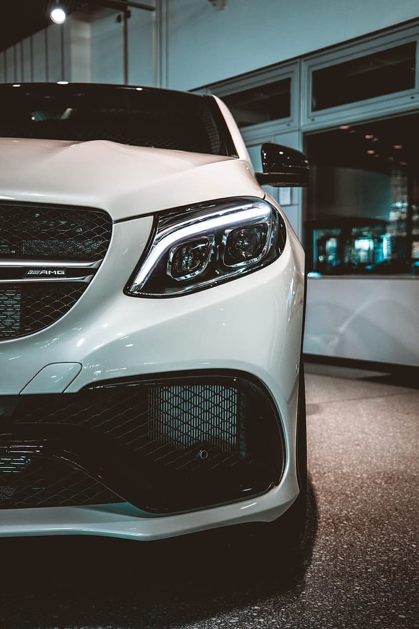 White Mercedes-AMG GLE 63 S Coupe LED headlight and chrome grille reflecting light in a modern showroom setting.
