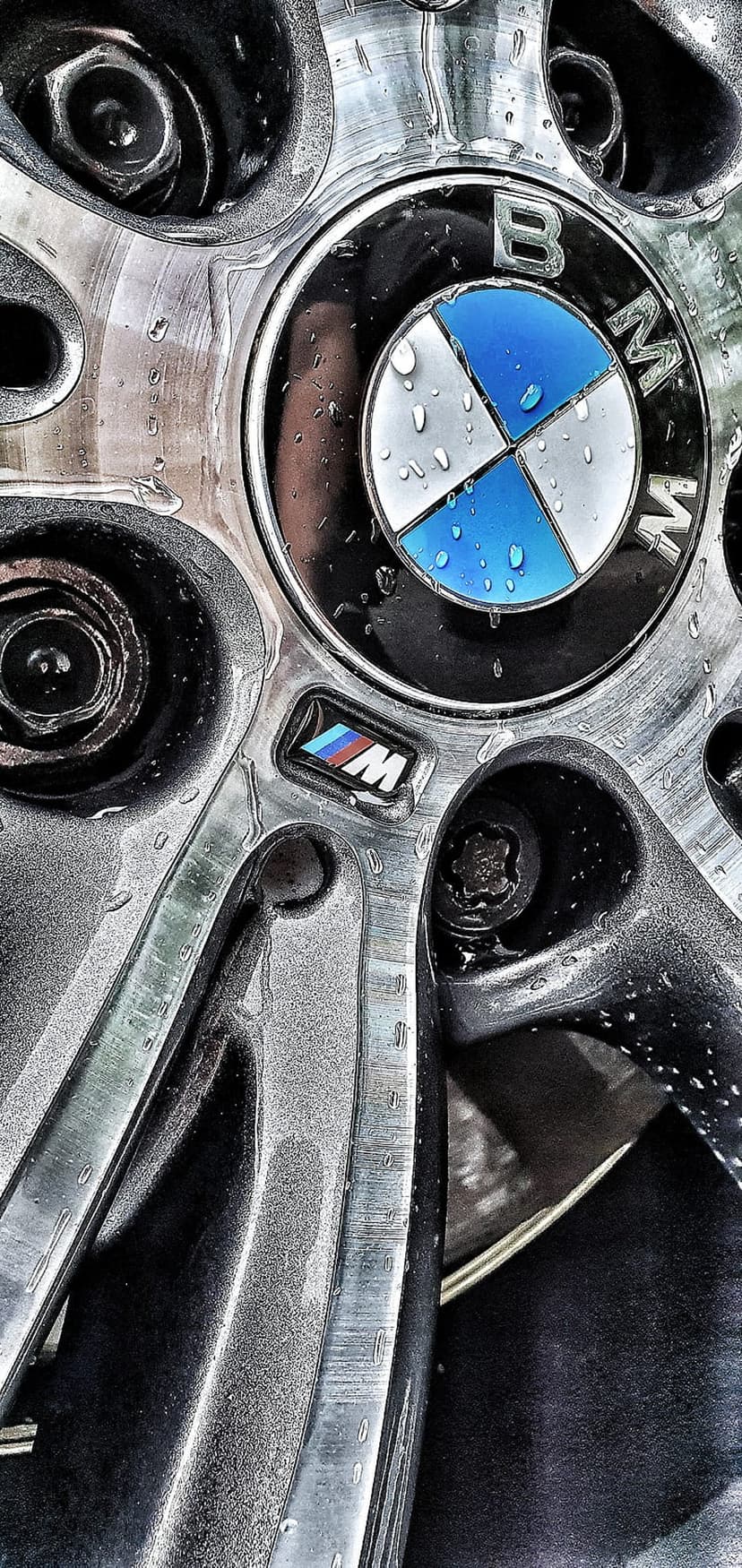 BMW M performance wheel with moisture droplets on silver alloy spokes and a central logo for mobile display.