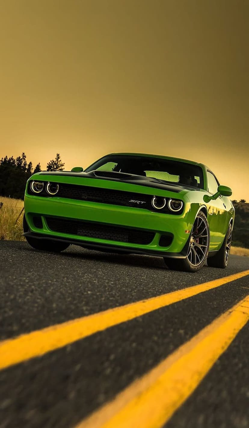 Lime green Dodge Challenger SRT Hellcat on an asphalt road with yellow lines during a warm golden hour sunset.
