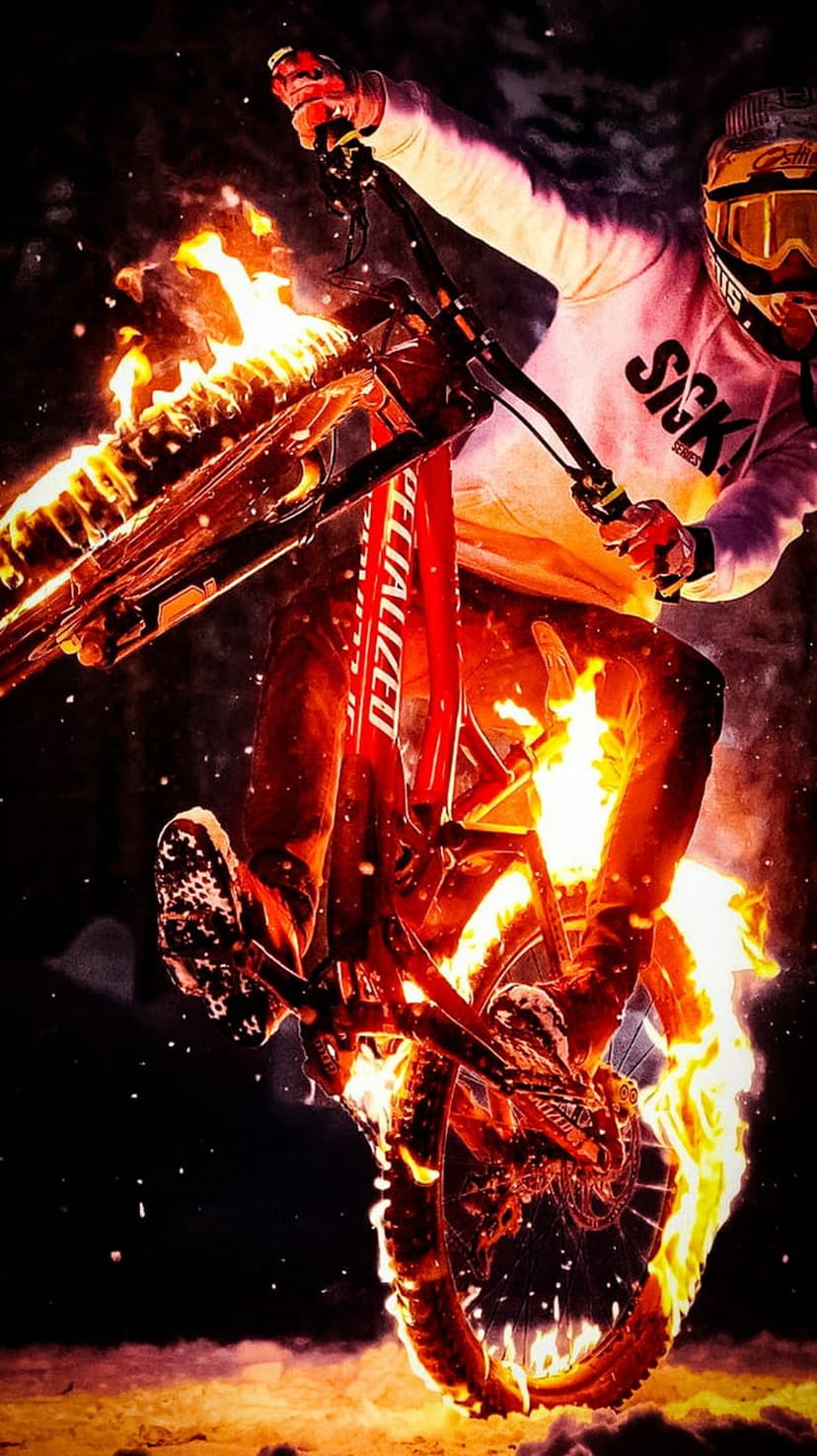 Cyclist leaping mid-air on a mountain bike engulfed in vivid orange flames against a dark, high-contrast background.