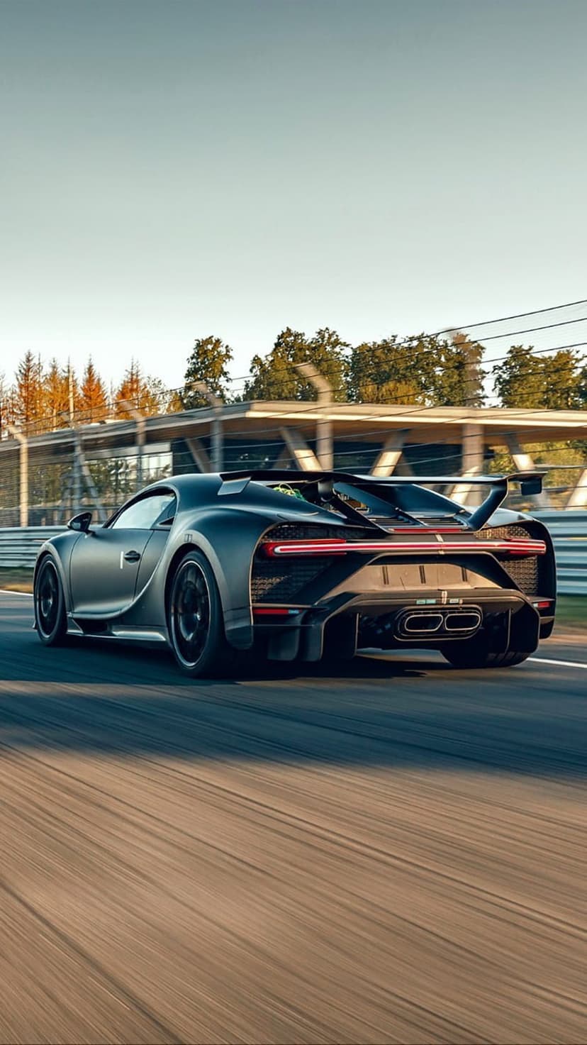 Bugatti Chiron Super Sport 300+ with matte black paint and glowing C-shaped taillights racing on a sunny track.