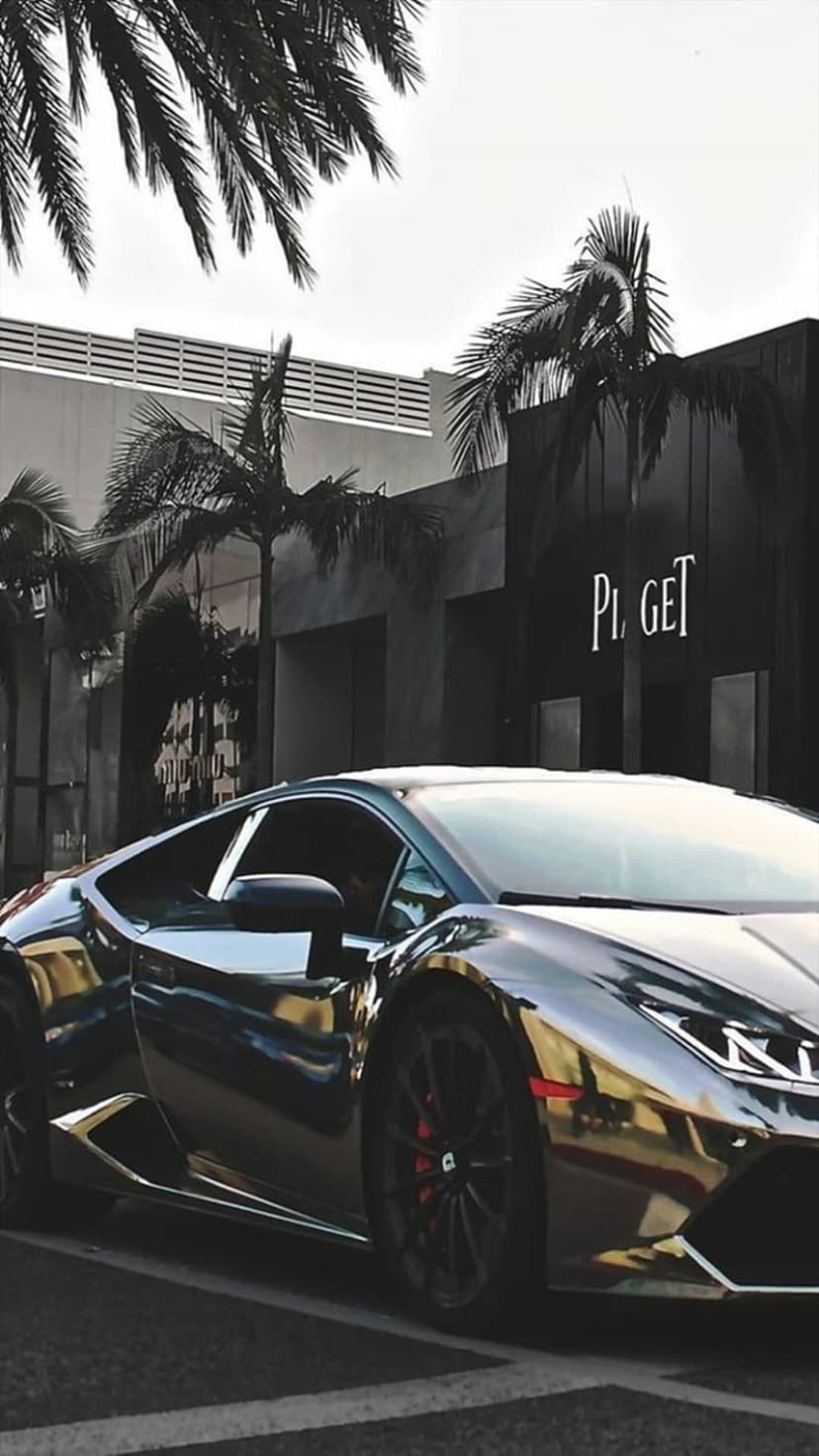 Chrome Lamborghini parked before a Piaget boutique with palm trees reflecting off the polished silver car body.