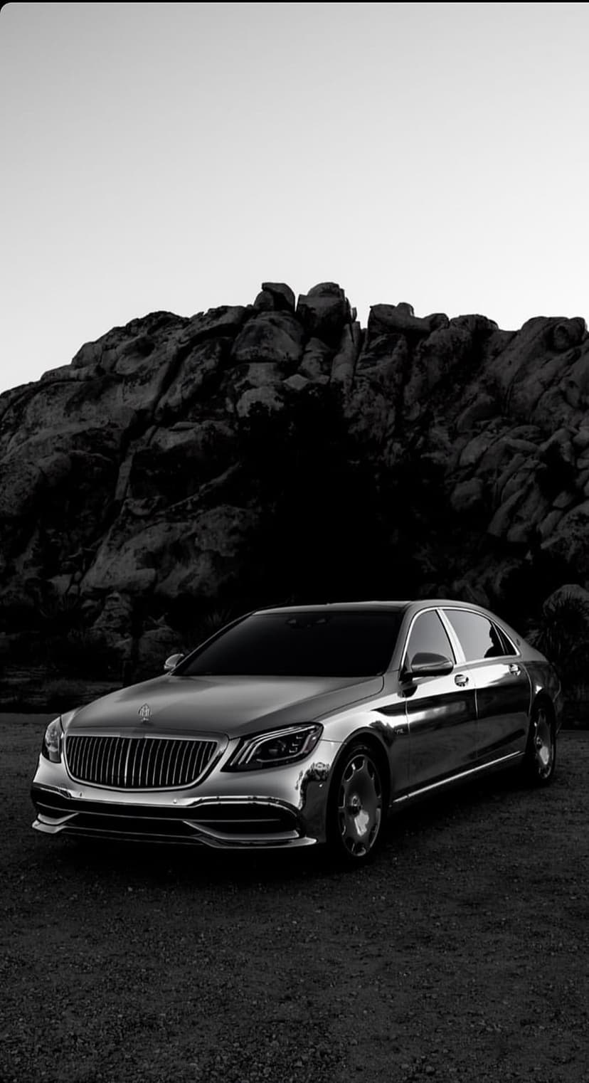 Luxury sedan with chrome accents parked before a rugged mountain range in a high-contrast black and white photograph.
