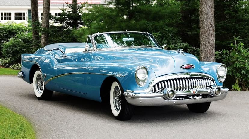 Sky blue 1953 Buick Skylark convertible on a driveway surrounded by green trees with chrome accents and whitewall tires.