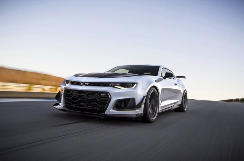 White Chevrolet Camaro ZL1 1LE with a black hood racing on a paved track with motion blur and clear blue sky.