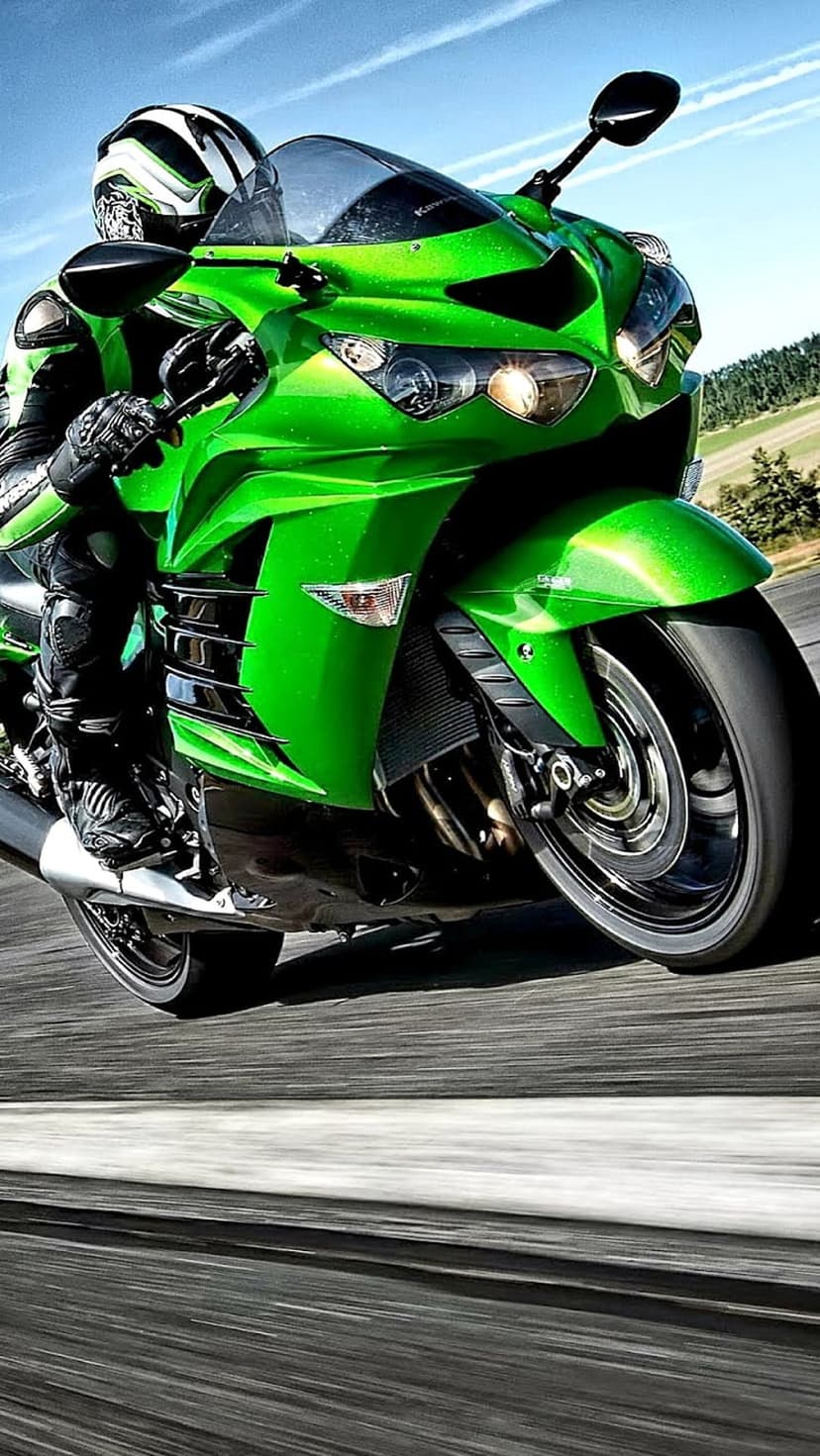 Rider on a green Kawasaki motorcycle leans into a sharp turn on a sun-drenched road with kinetic motion blur.