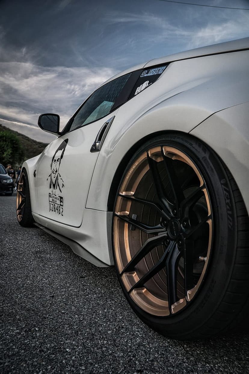 Nissan 370Z with white paint and bronze wheels parked under a dramatic, dark cloudy sky at a low angle.
