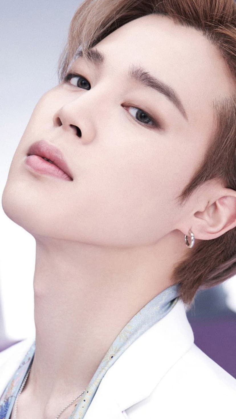 Park Jimin of BTS features light brown hair and a silver earring in a soft close-up portrait with a white jacket.