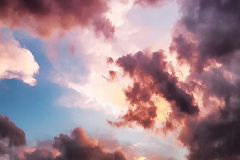 Fluffy pink and purple clouds fill a sunset sky with vibrant orange highlights and patches of clear blue light.
