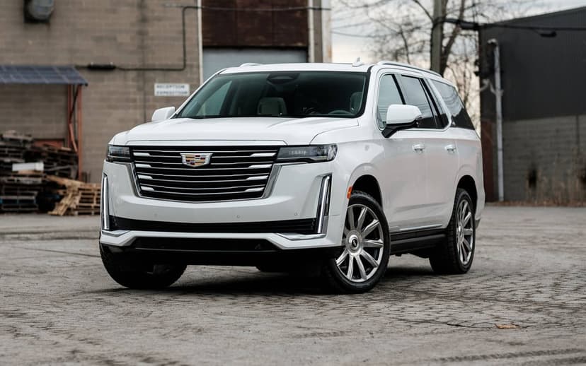 White Cadillac Escalade luxury SUV parked in an industrial lot with a large chrome grille and silver wheels.