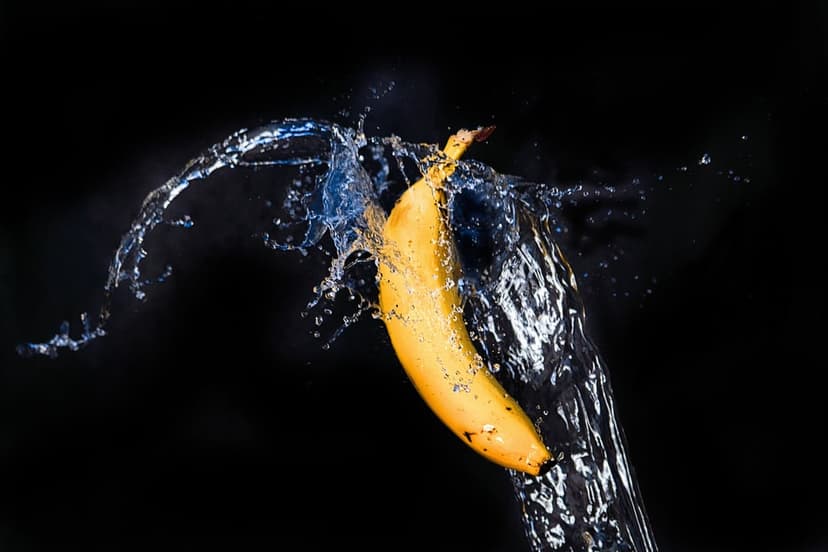 Yellow banana colliding with an explosive water splash against a solid black background in high-speed detail.