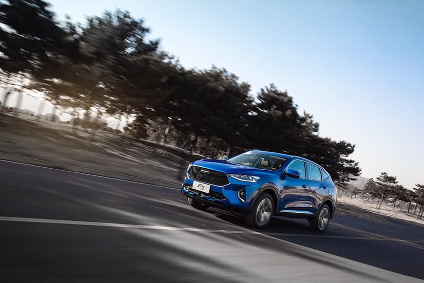Blue Haval F7 SUV driving fast on a sunlit asphalt road with heavy motion blur in the background trees.