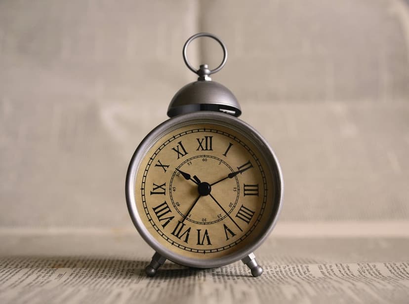 Vintage silver alarm clock with Roman numerals on newsprint under soft light for a vertical screen display.