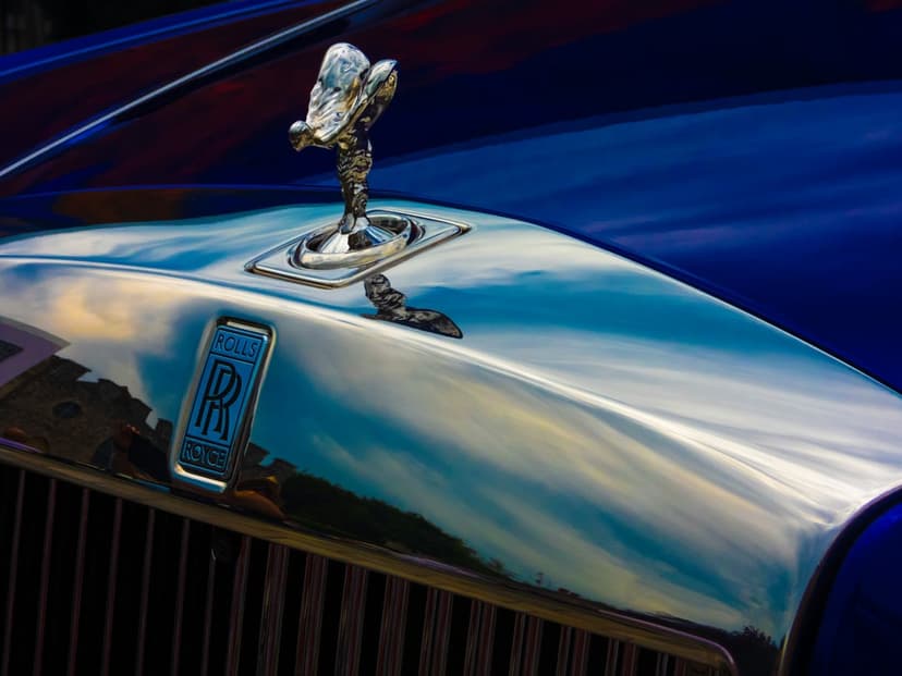 Spirit of Ecstasy silver hood ornament on a polished blue Rolls-Royce with crisp metallic reflections and bokeh.
