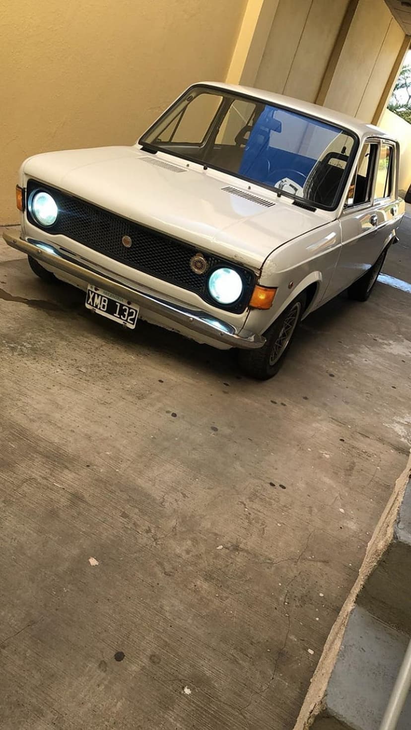 Fiat 128 sedan in white parked by a yellow wall with chrome bumpers and classic headlights on a concrete floor.