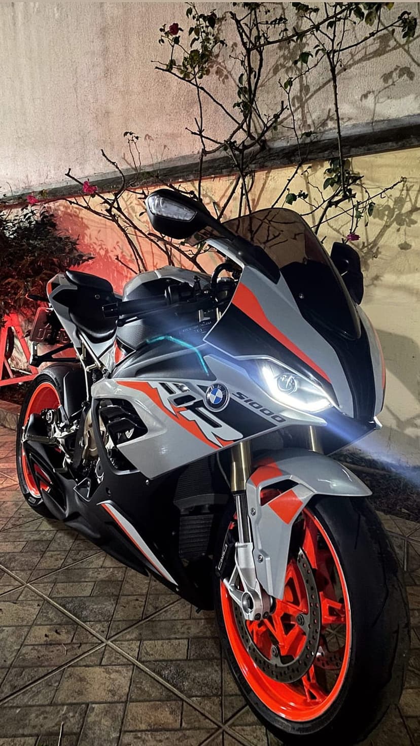 BMW S1000RR sportbike with glowing orange wheels and headlights parked on tiles near a textured wall.