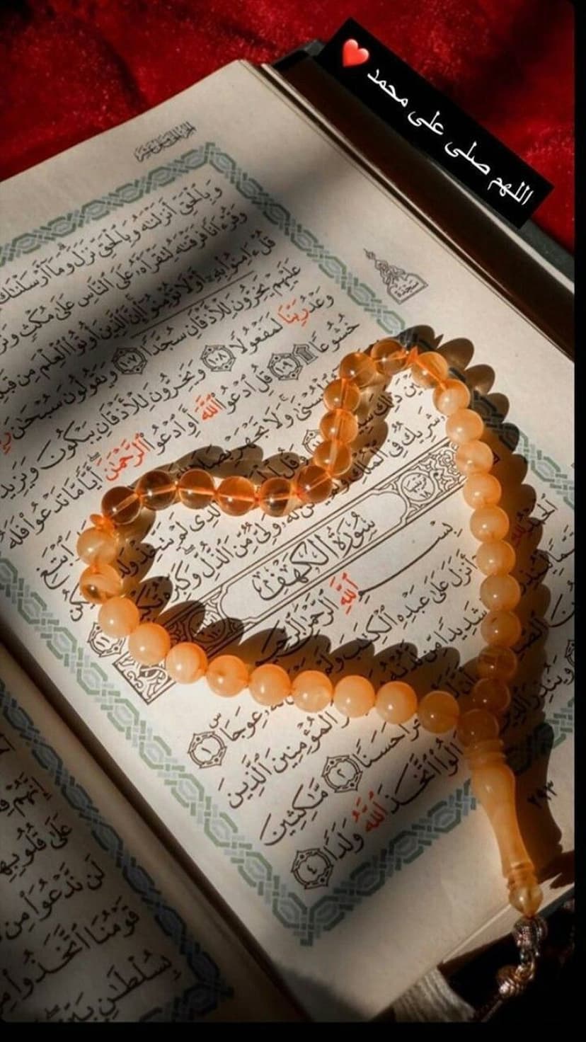 Amber prayer beads draped over an open Quran with Arabic script illuminated by warm, glowing natural light.