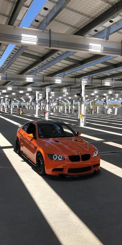 Orange BMW M3 parked under solar panel carport