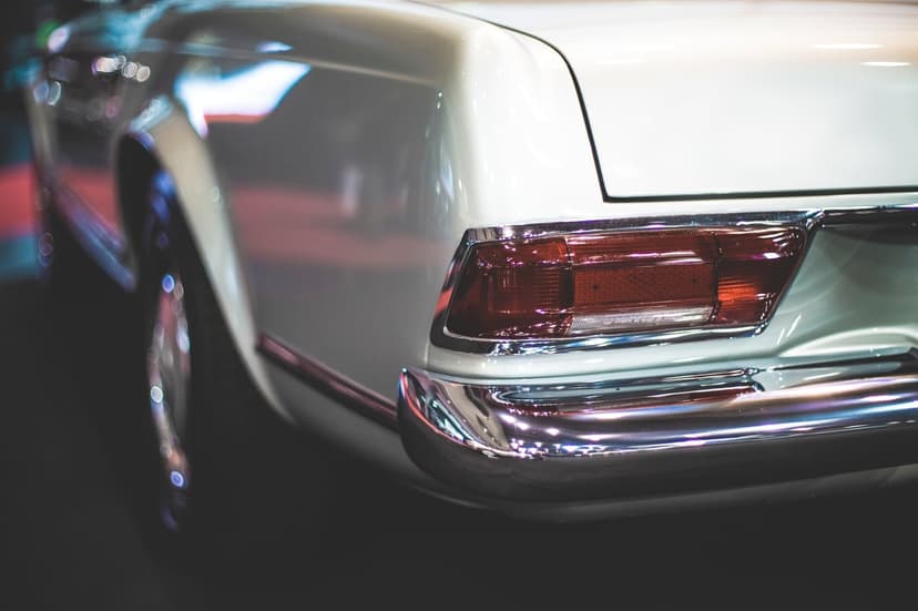 White vintage car rear bumper with polished chrome trim and a rounded red taillight assembly in sharp focus.