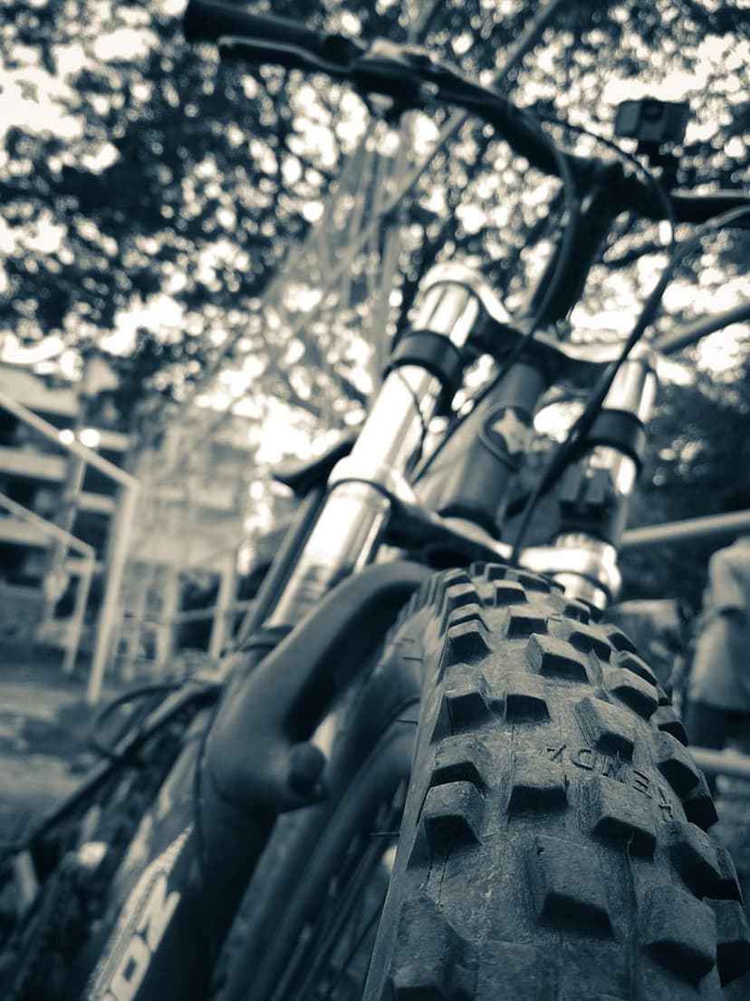 Knobby mountain bike tire and handlebars shown from a low-angle in a dramatic monochrome urban setting.