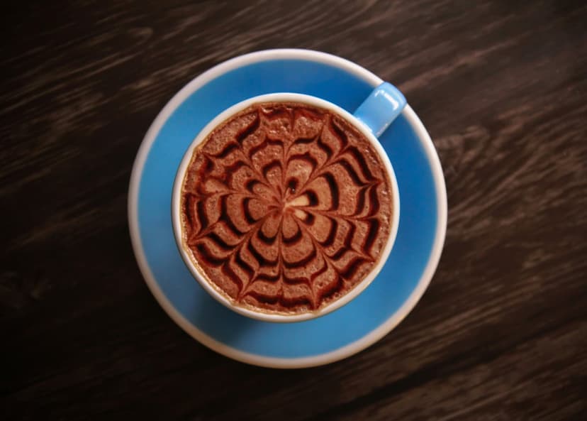 Chocolate latte art in a white cup on a blue saucer over a dark wood table seen from a top-down view.