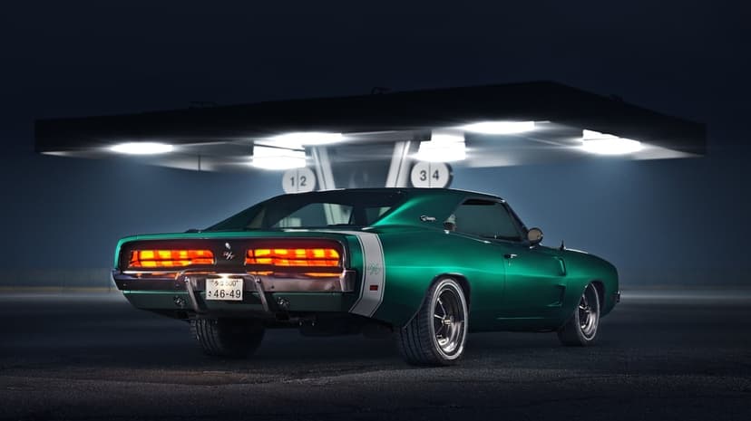 Rear view of a dark green Dodge Charger with glowing red taillights parked under bright gas station lights at night.