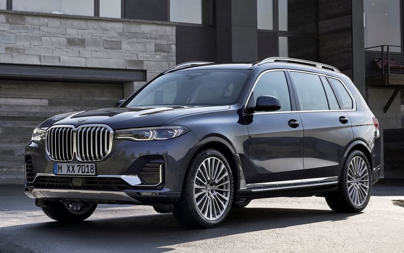 Dark blue BMW X7 SUV parked in front of a modern stone building with large chrome kidney grille and alloy wheels.